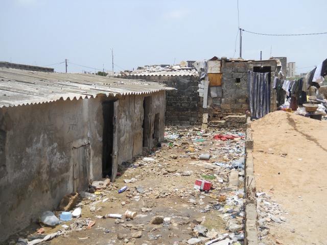 On the left of the image, an abandoned house half buried in a mix of sand, compressed garbage and rubble. To the right, a deposit of sand for a house to soon be built over the embankment, 18/07/2012